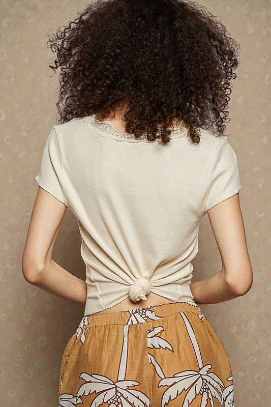 Person wearing a beige top with a knot detail and a patterned skirt against a neutral background