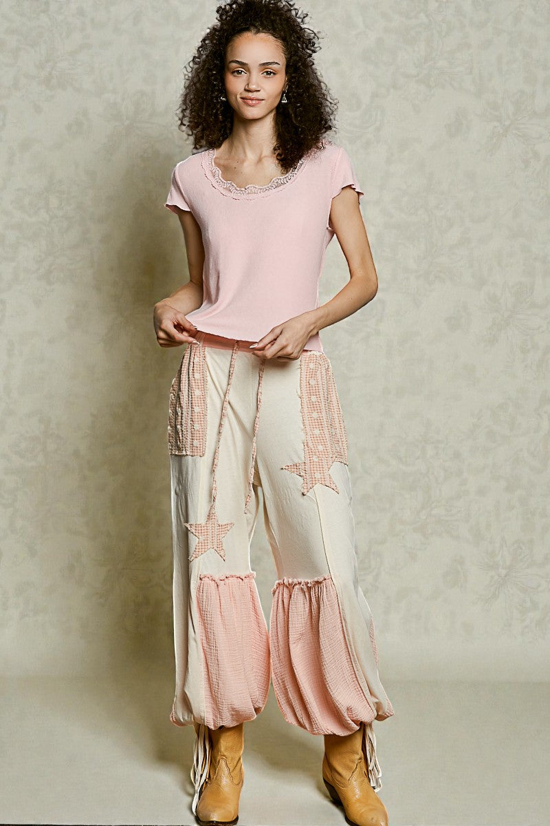 Woman wearing a pink top and white pants with pink accents against a neutral background