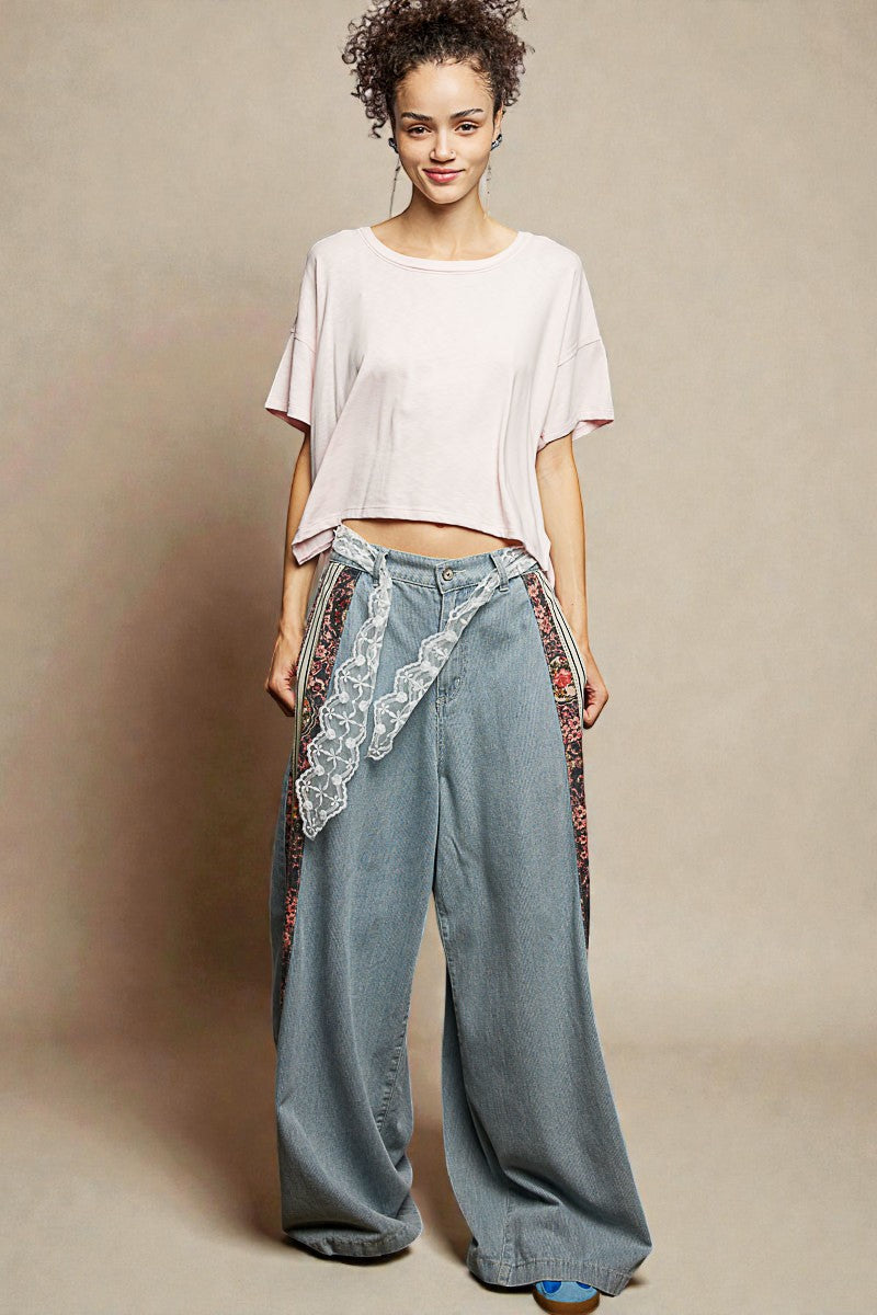 Woman wearing a light pink top and wide-leg jeans with lace details on a beige background