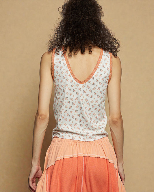 Person wearing a floral tank top and orange skirt against a beige background