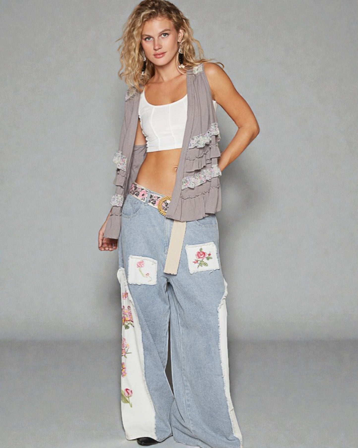 Woman wearing a stylish outfit with a long cardigan, white top, and floral pants on a gray background