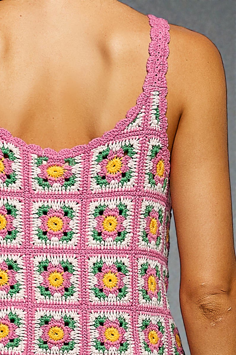 Close-up of a person wearing a pink crochet dress with floral patterns on a gray background