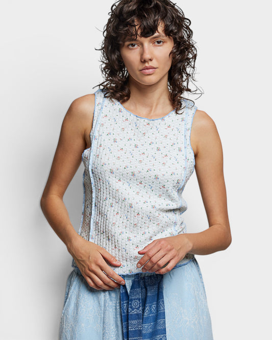 Woman wearing a light blue sleeveless top with a subtle pattern against a plain background