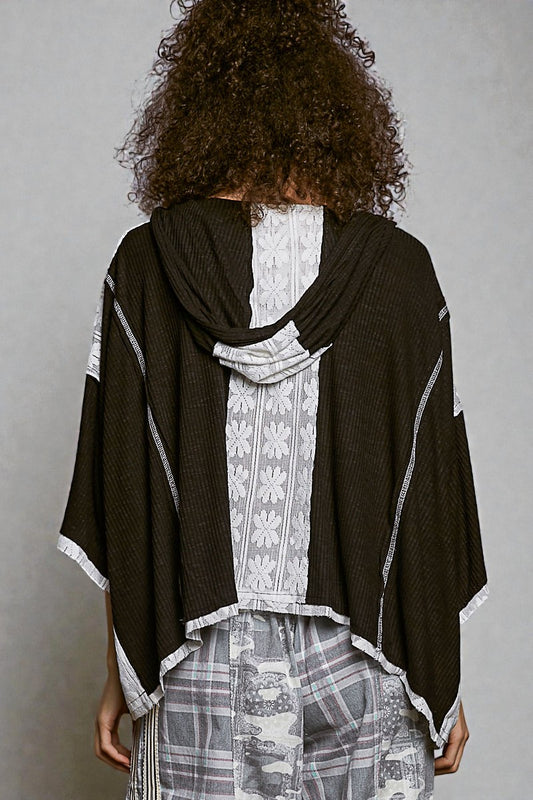 Person wearing a black poncho over a patterned outfit against a gray background