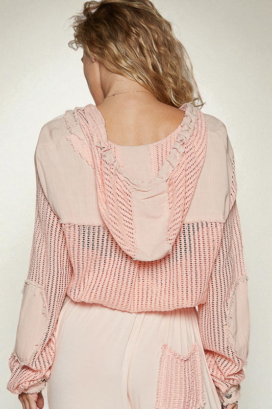 Person wearing a pink knitted cardigan over a light-colored shirt and pants on a plain background