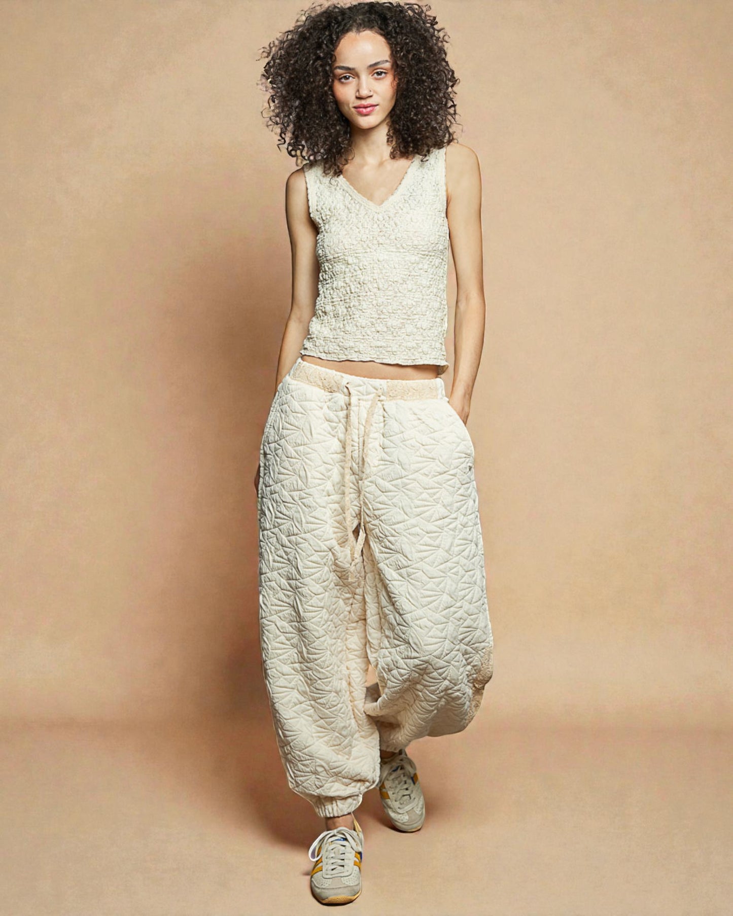 Woman wearing a light-colored sleeveless top and wide-leg pants against a beige background