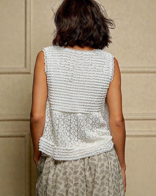 Woman wearing a textured sleeveless top against a beige wall
