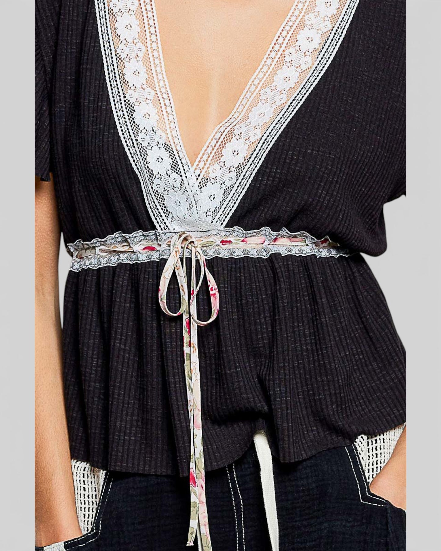 Black top with lace details and a floral belt on a neutral background