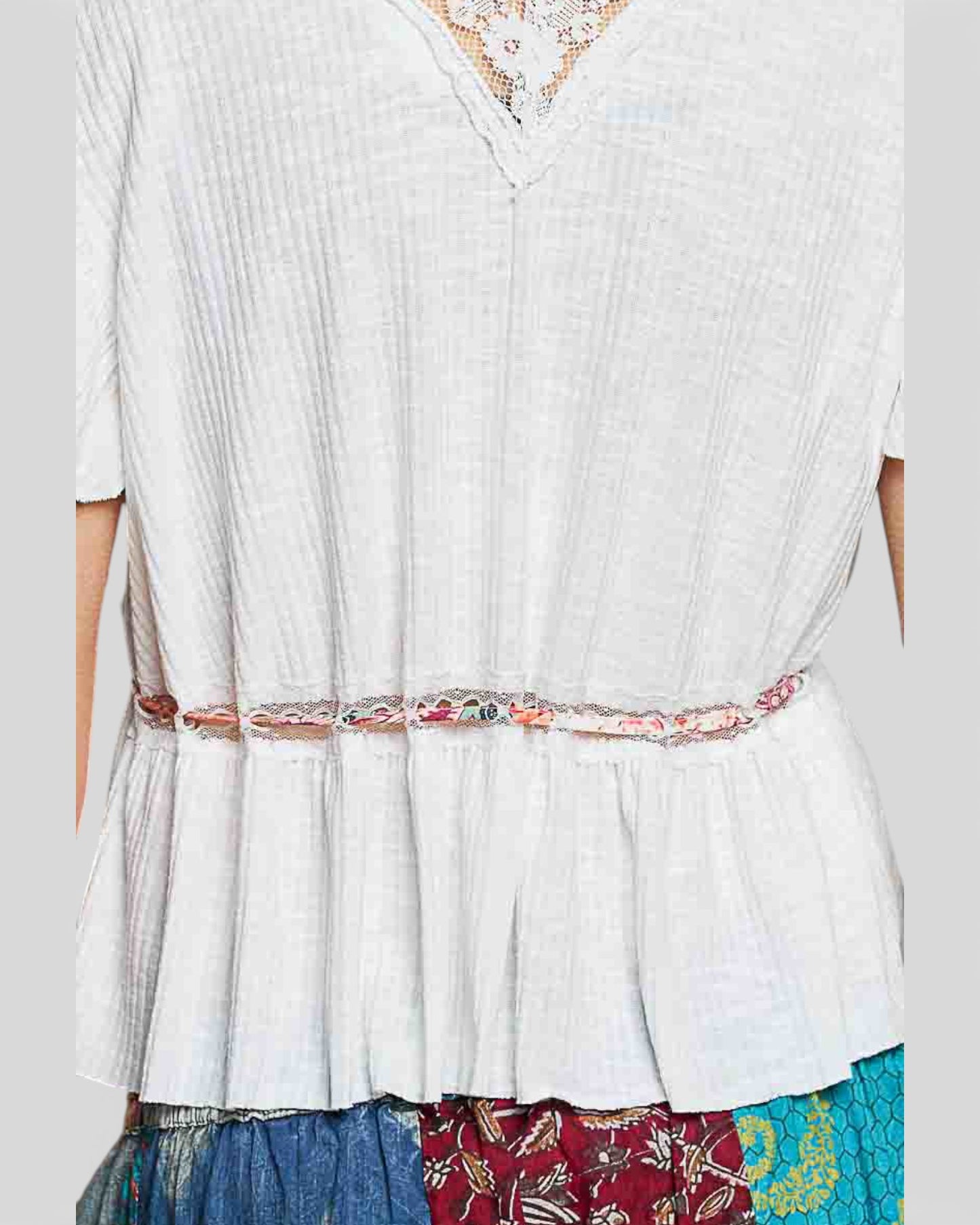 White blouse with a colorful belt and patterned skirt on a plain background