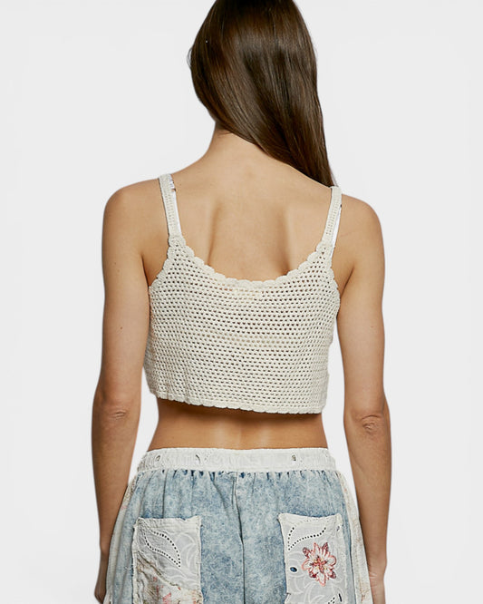 Woman wearing a white crochet top and denim skirt with floral patterns on a light gray background