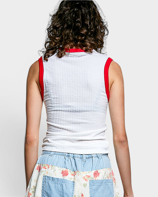 Person wearing a white sleeveless top with red straps on a plain background