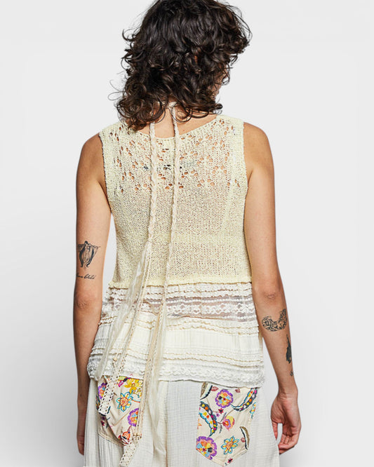 Person wearing a light-colored sleeveless top with a floral scarf, on a plain background