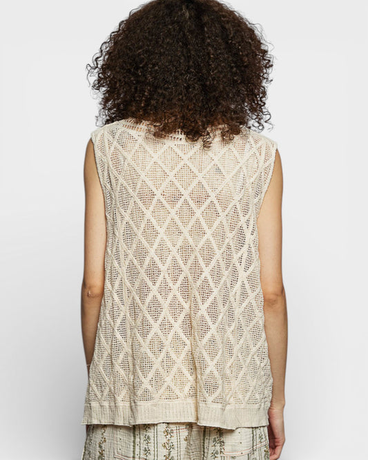 Woman wearing a beige sleeveless top with a diamond pattern on a white background