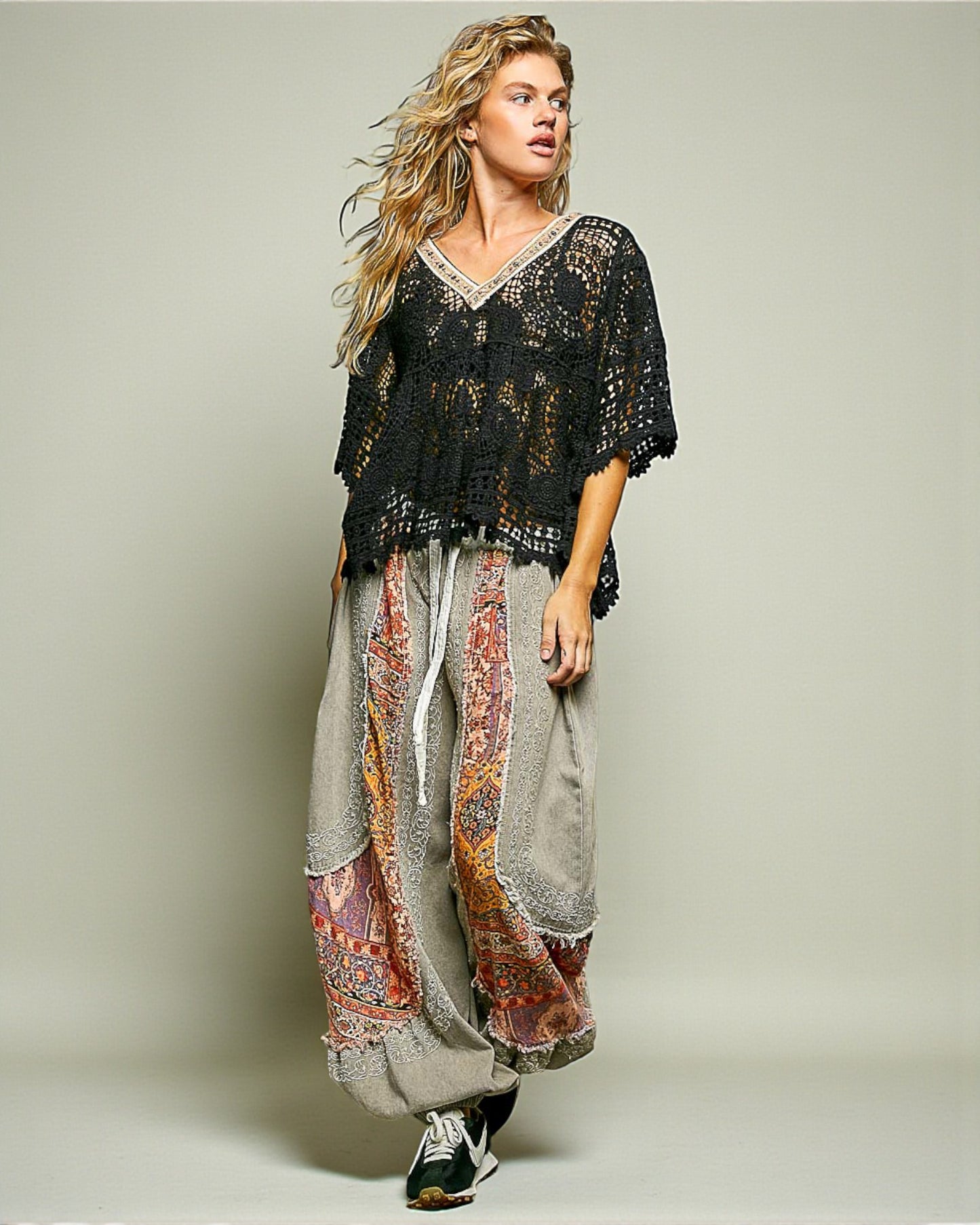 Woman wearing a black lace top and patterned harem pants on a plain background