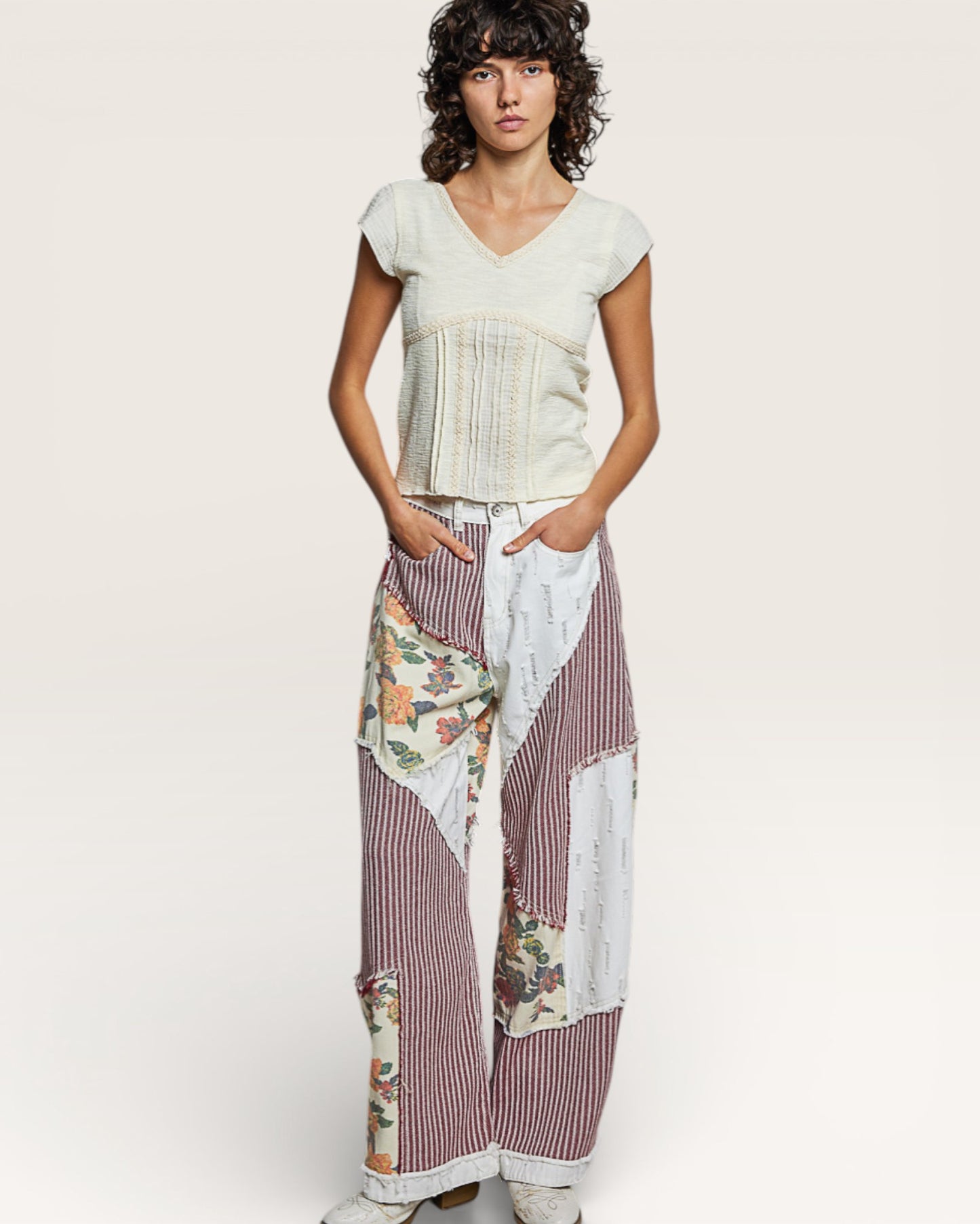 Woman wearing a white top and floral patchwork pants on a plain background