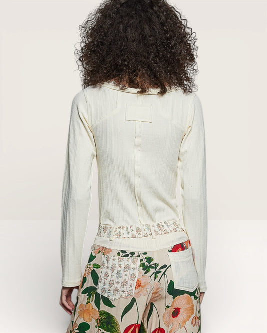 Person wearing a white long-sleeve top and floral skirt on a plain background