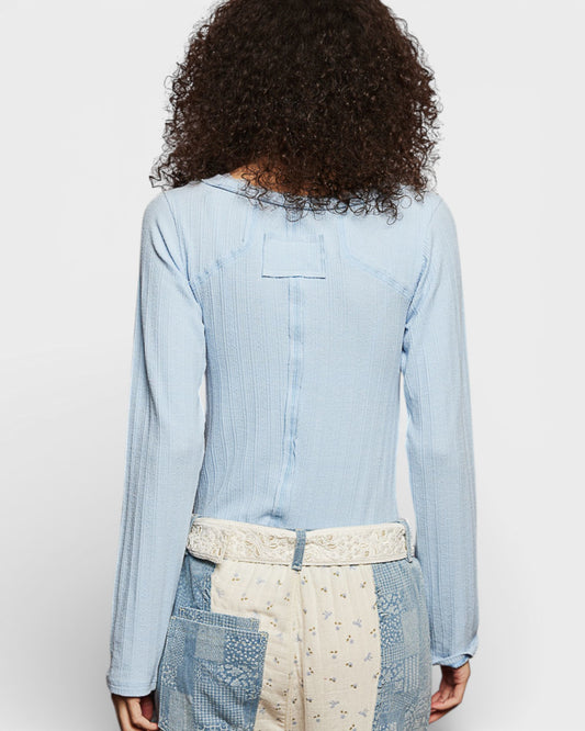 Person wearing a light blue denim shirt with a white apron on a plain background