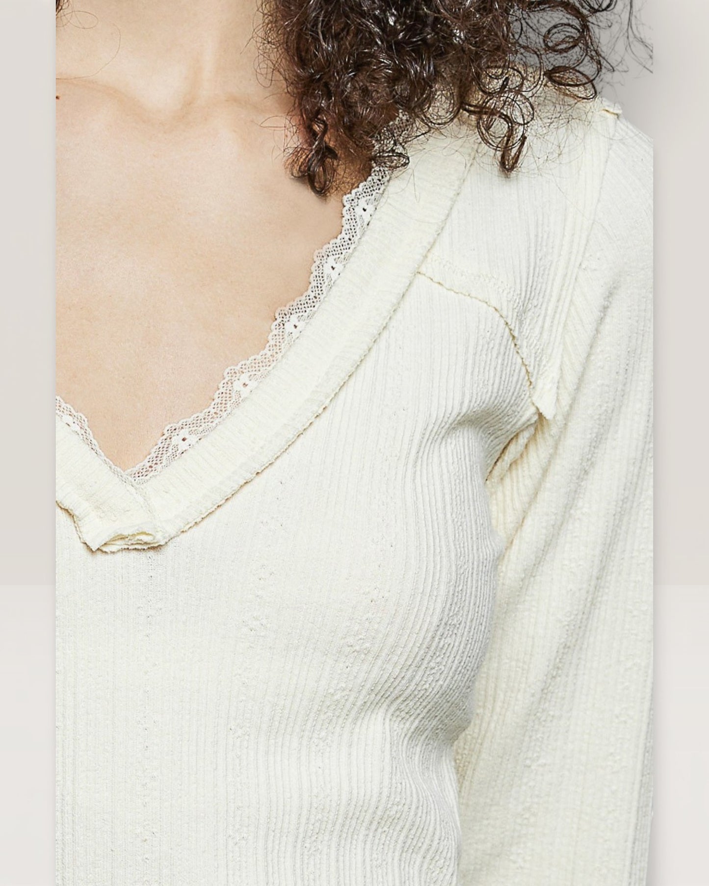 Close-up of a person wearing a light-colored top with lace trim on a plain background