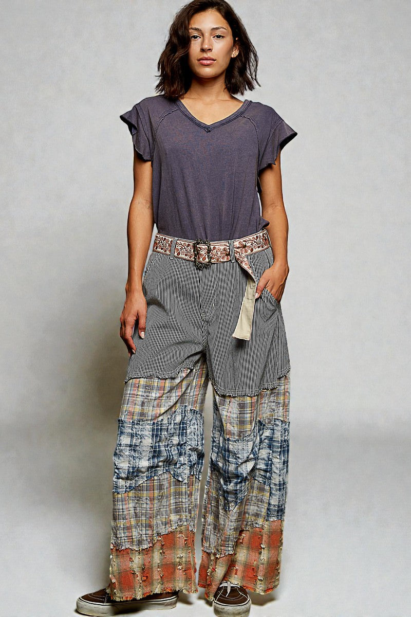 Woman wearing a gray top and plaid pants with a belt on a plain background