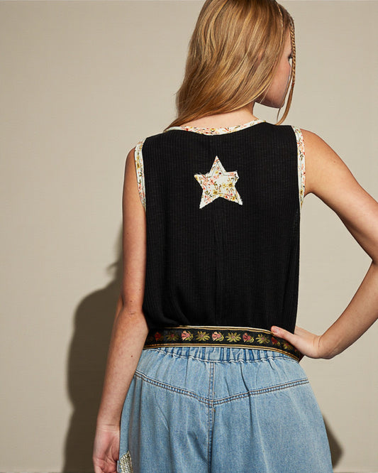 Woman wearing a black sleeveless top with a star design and blue jeans against a beige background