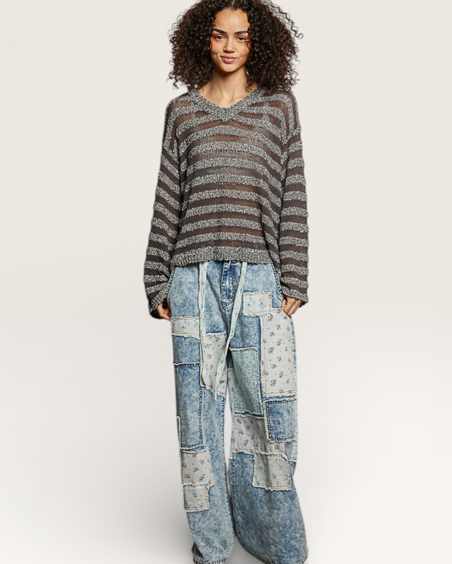 Person wearing a striped sweater and patchwork jeans on a white background