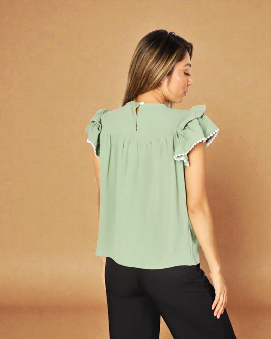 Woman wearing a light green blouse with ruffled sleeves against a brown background