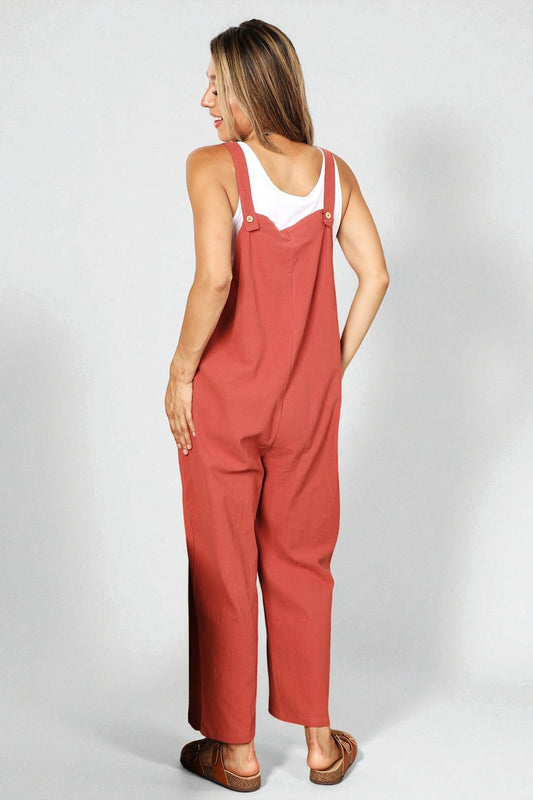 Woman wearing red overalls and a white tank top on a plain background