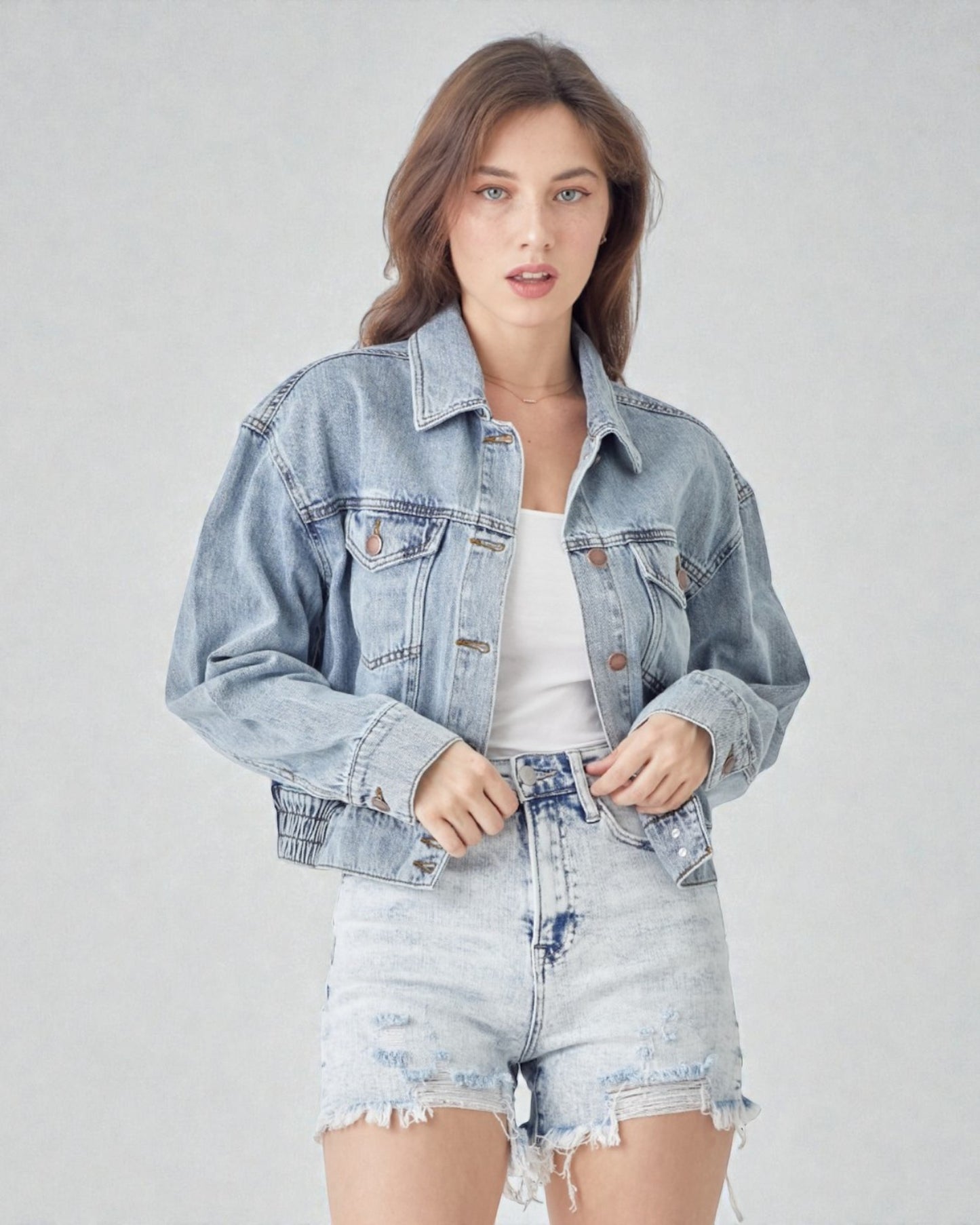 Woman wearing a light blue denim jacket and shorts on a gray background