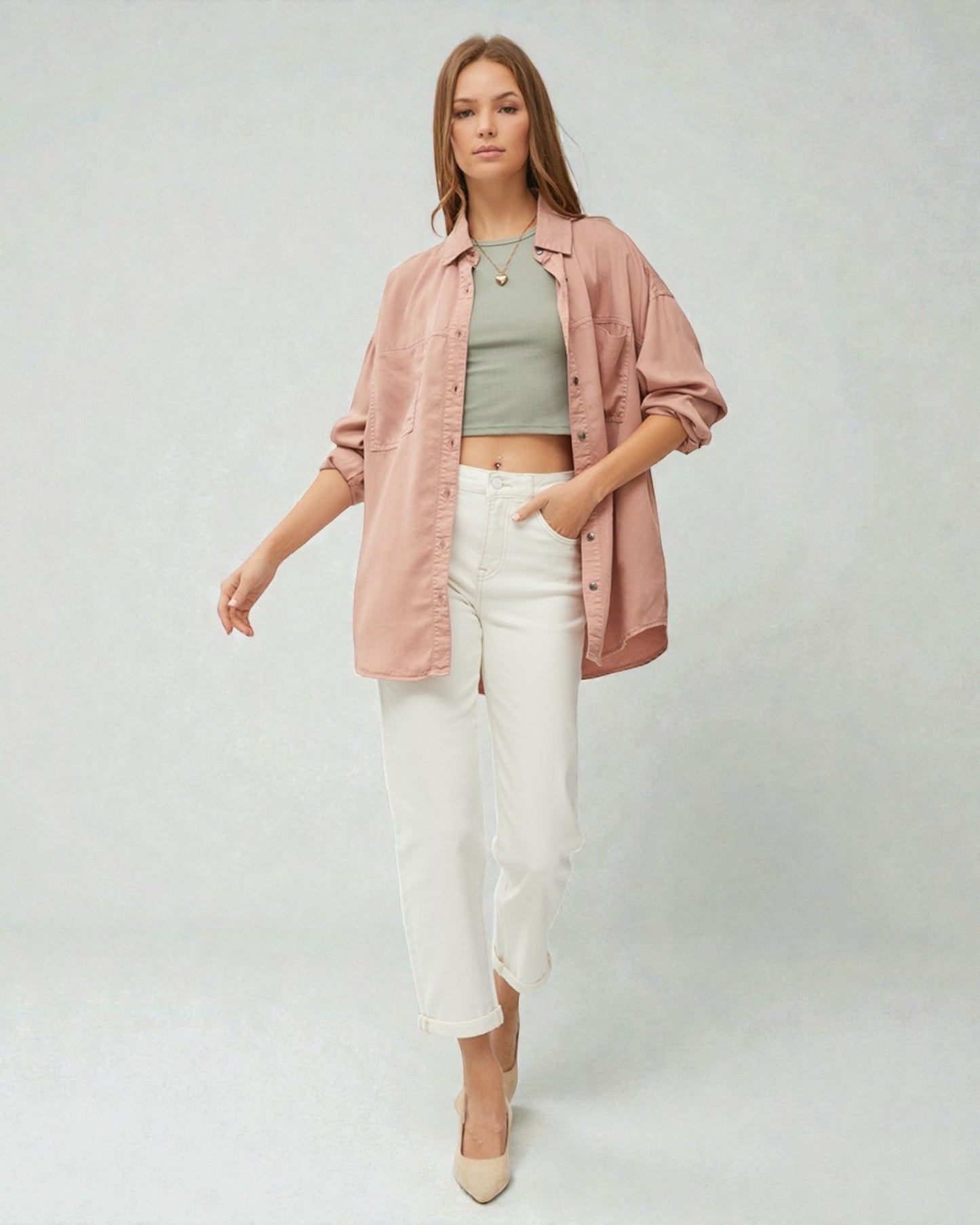 Woman wearing a pink shirt, green top, and white pants on a plain background