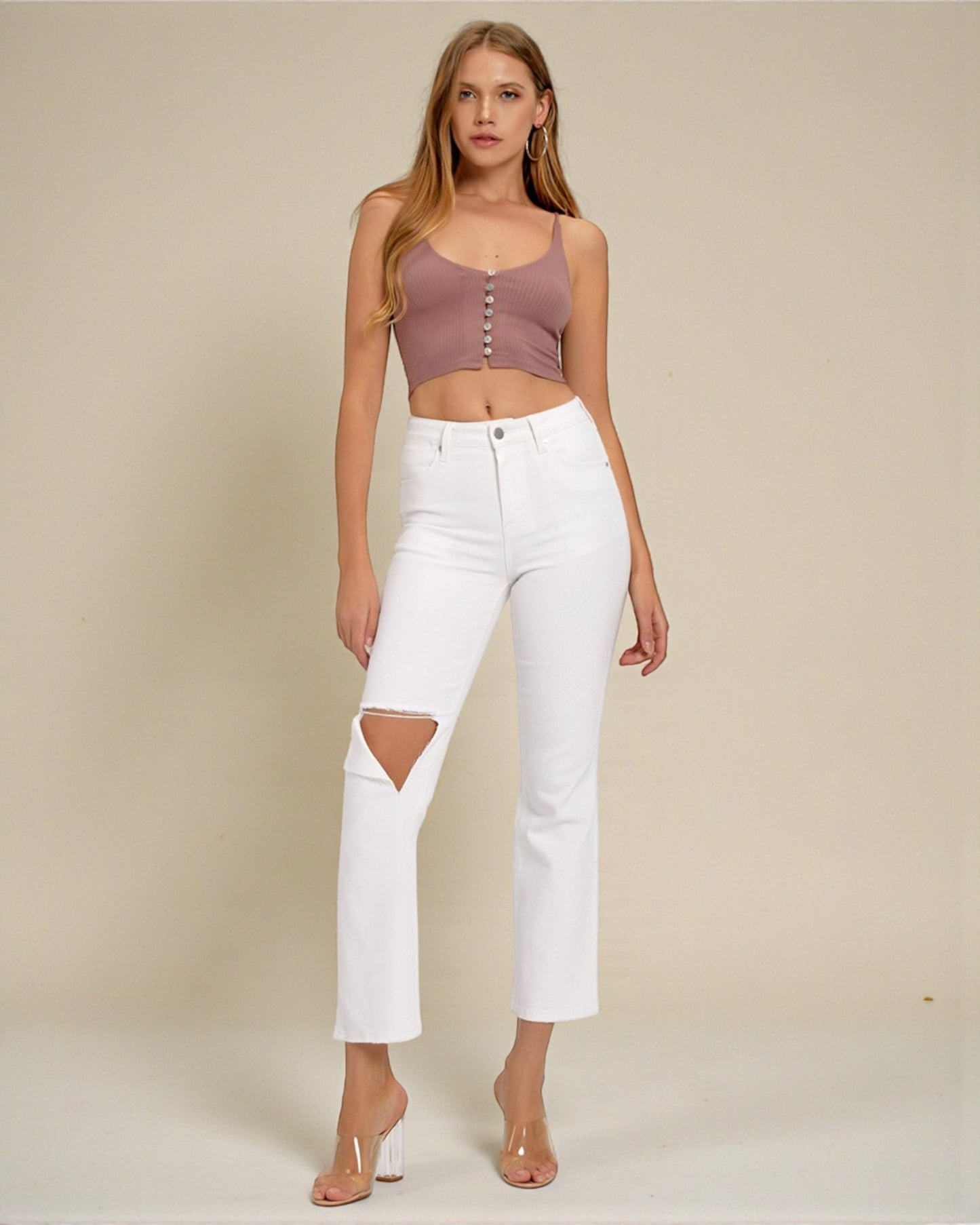 Woman wearing a mauve crop top and white jeans with cut-out design on a beige background