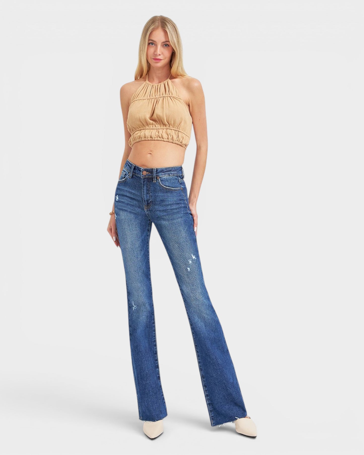 Woman wearing a beige top and blue jeans on a white background