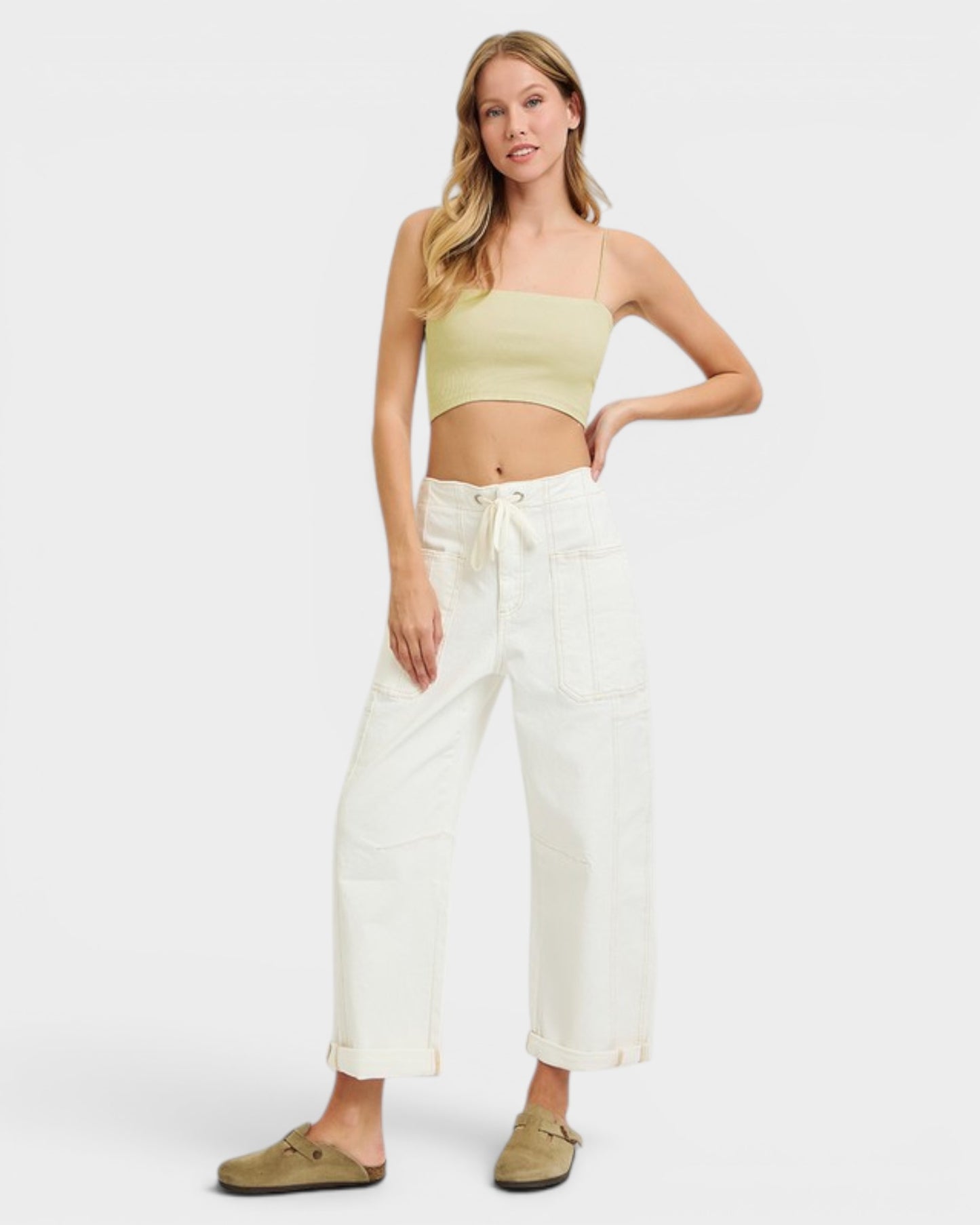 Woman wearing a light green crop top and white pants on a white background