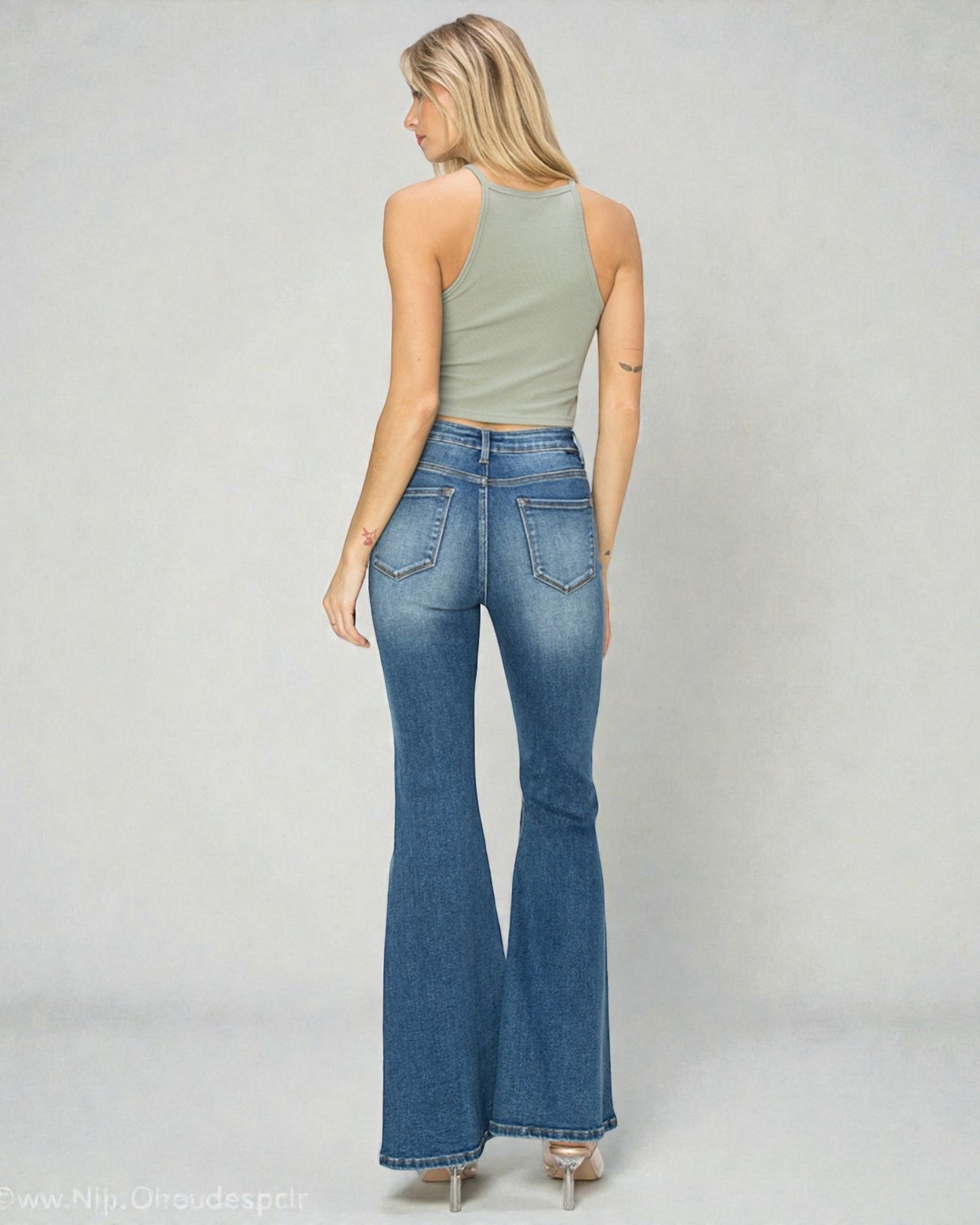 Woman wearing blue flared jeans and a green top on a plain background