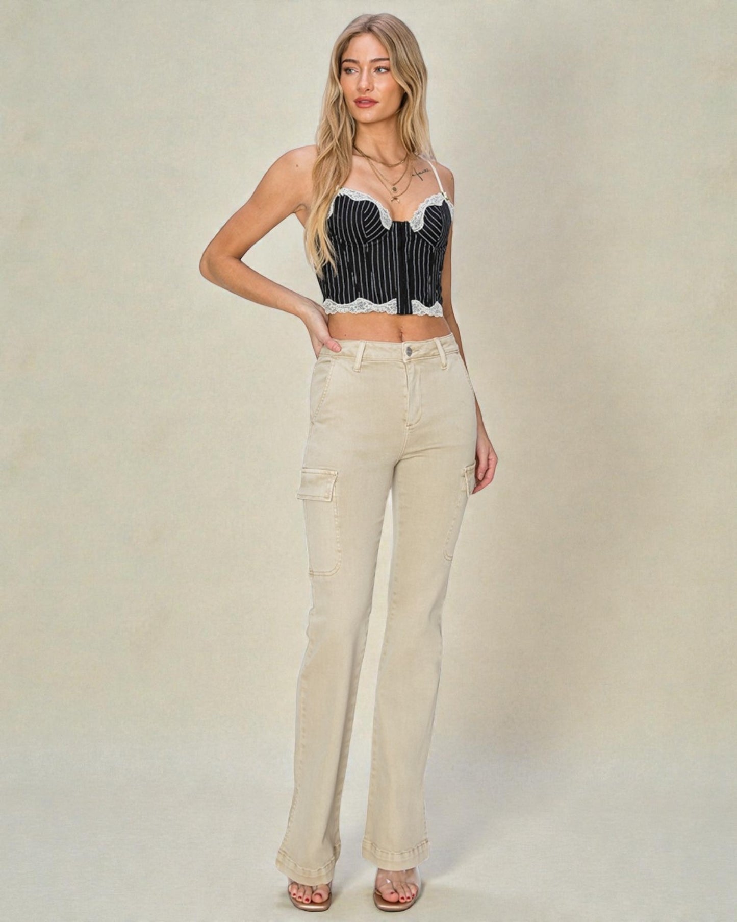 Woman wearing a black and white striped crop top and beige flared jeans on a plain background