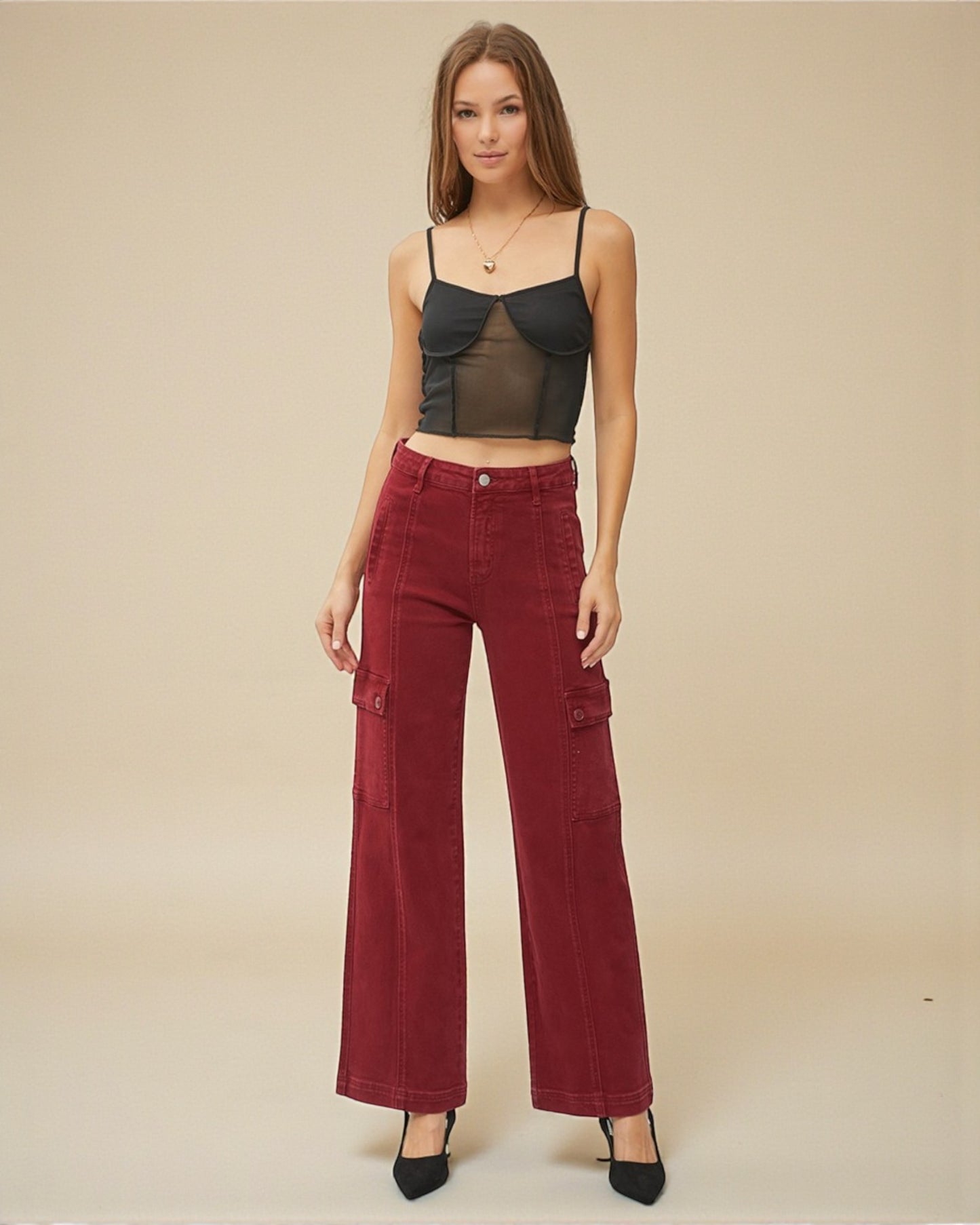 Woman wearing a black top and red pants against a beige background