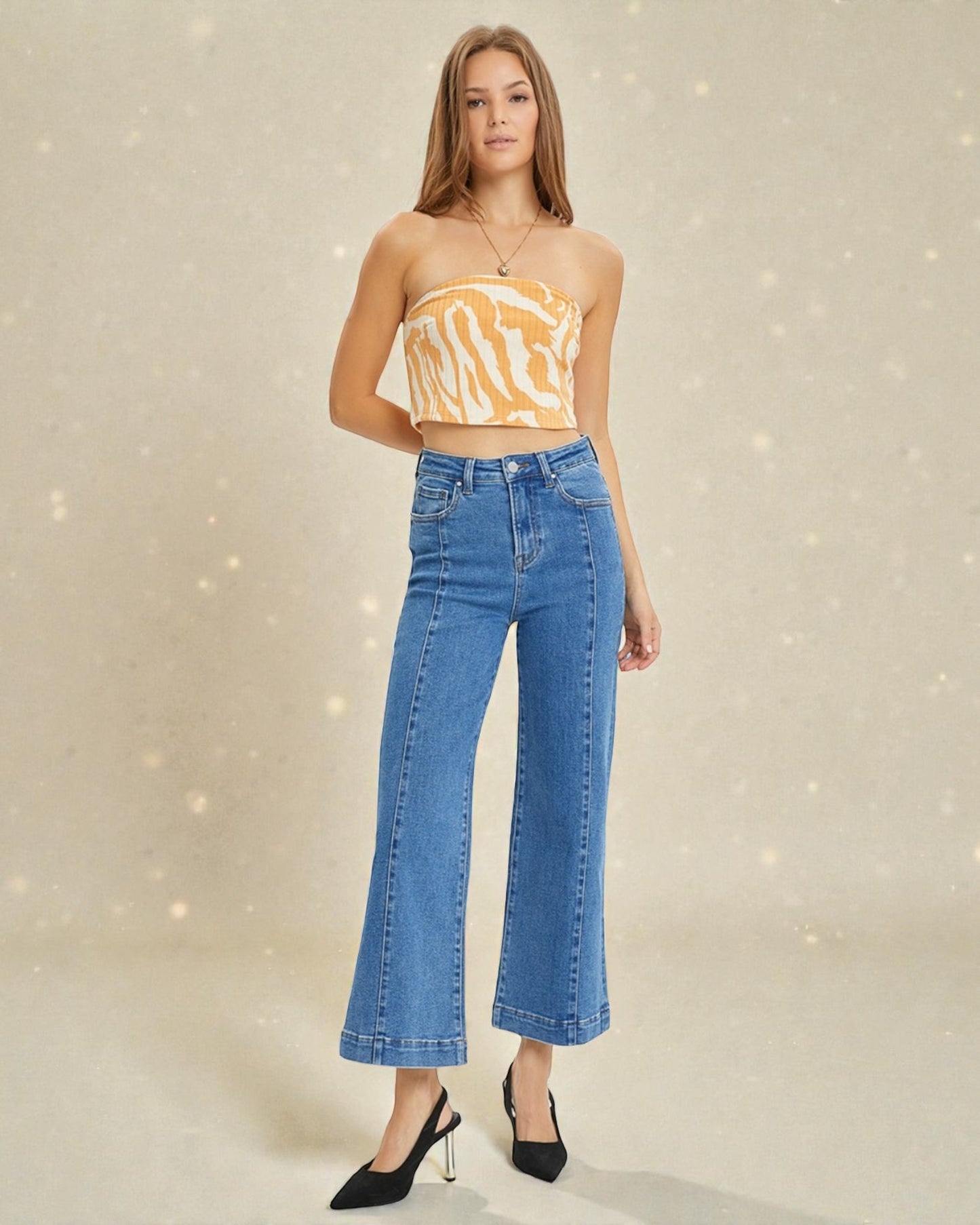 Woman wearing a strapless yellow top and blue jeans on a beige background