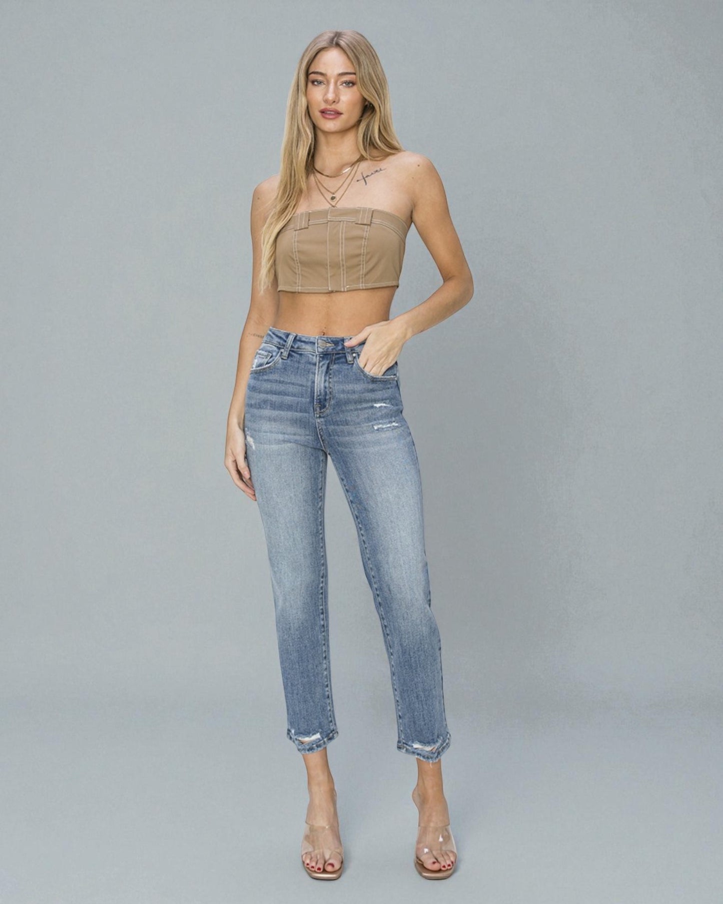 Woman wearing a beige crop top and blue jeans on a gray background