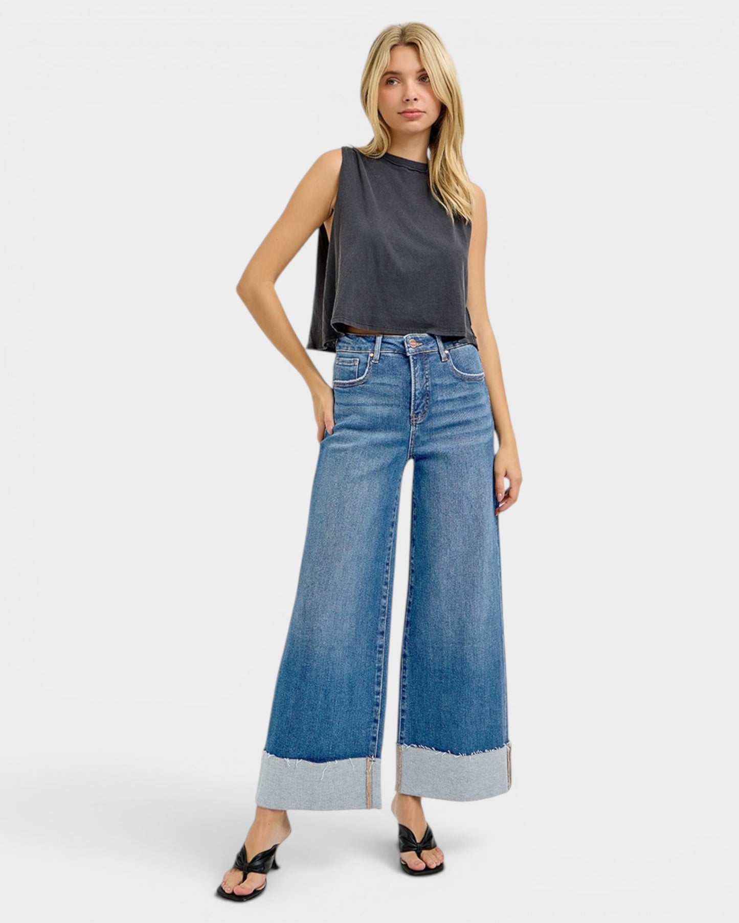 Woman wearing a dark gray sleeveless top and blue wide-leg jeans on a white background