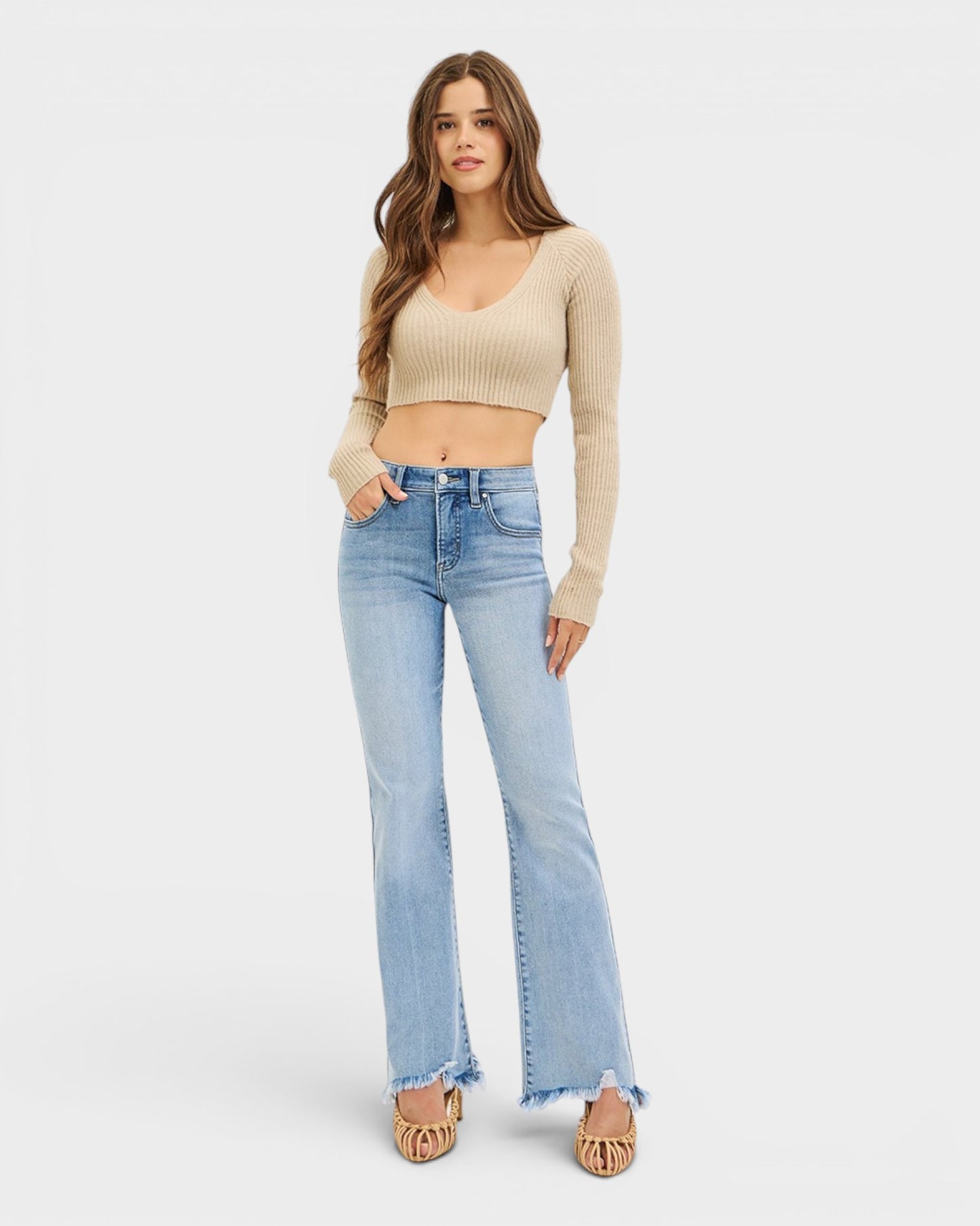 Woman wearing a beige crop top and light blue jeans on a white background