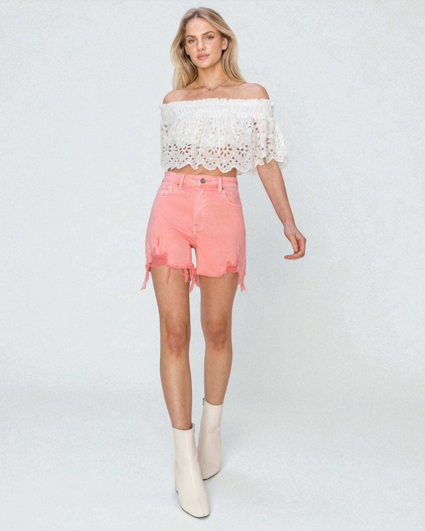 Woman wearing a white lace top and pink shorts on a white background