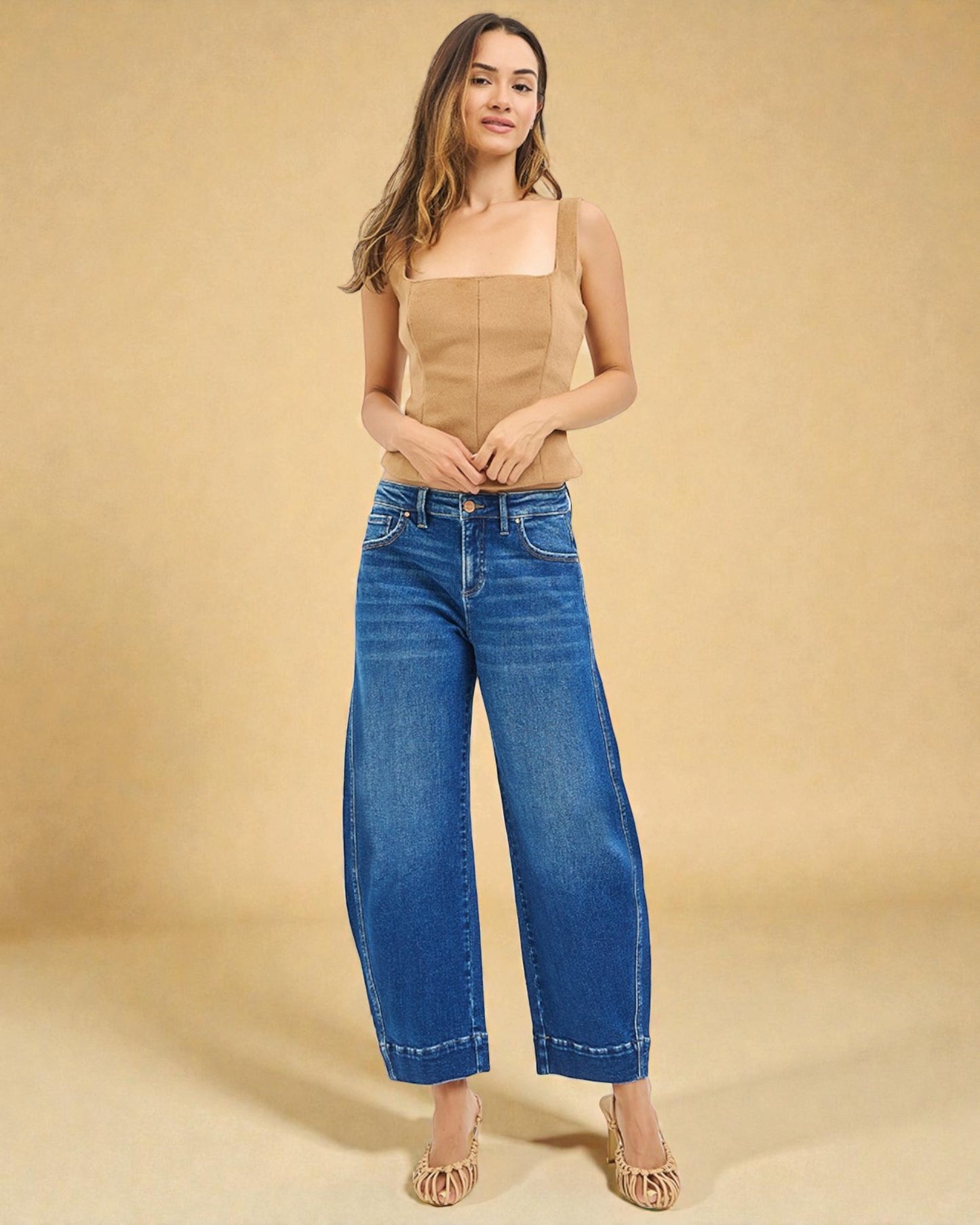 Woman wearing a beige top and blue jeans against a beige background
