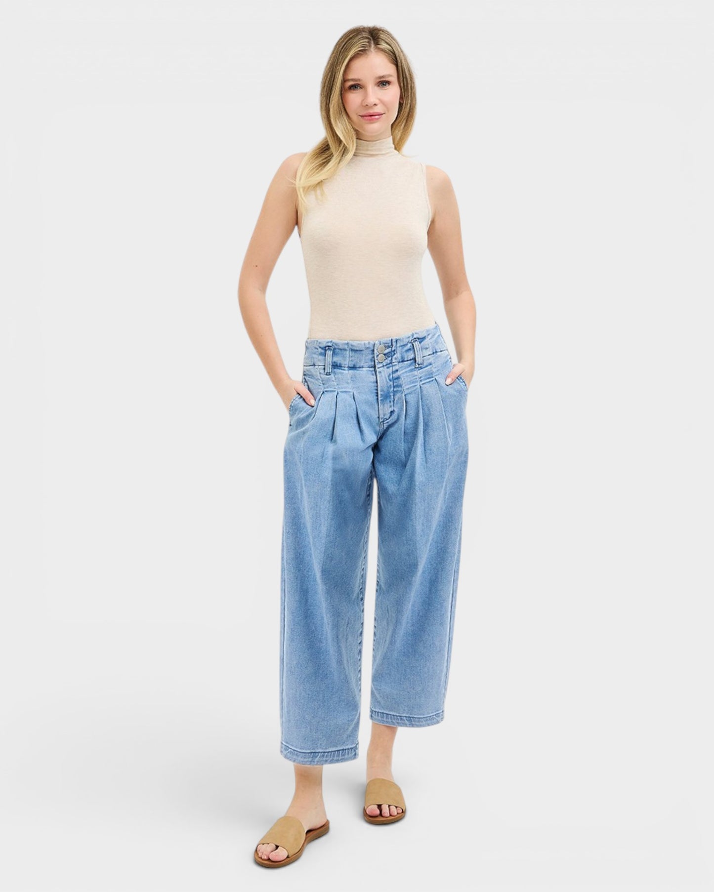 Woman wearing light blue jeans and a beige top on a white background