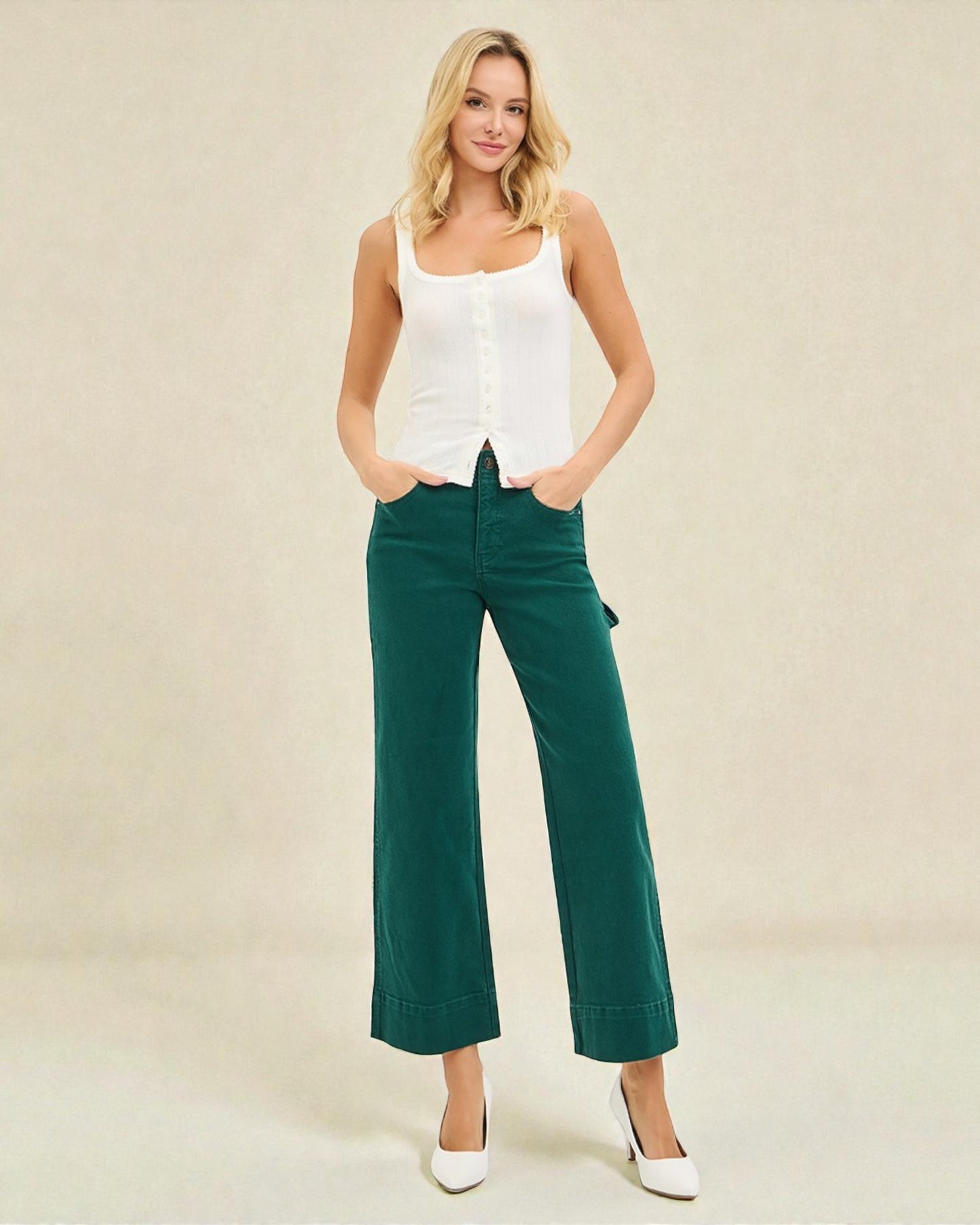 Woman wearing a white tank top and green pants on a beige background