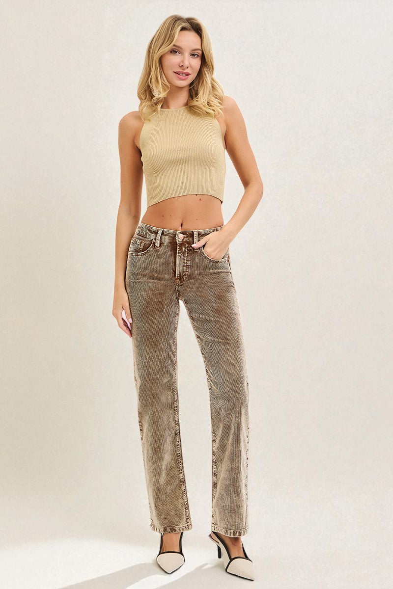 Woman wearing a beige sleeveless top and patterned jeans on a plain background