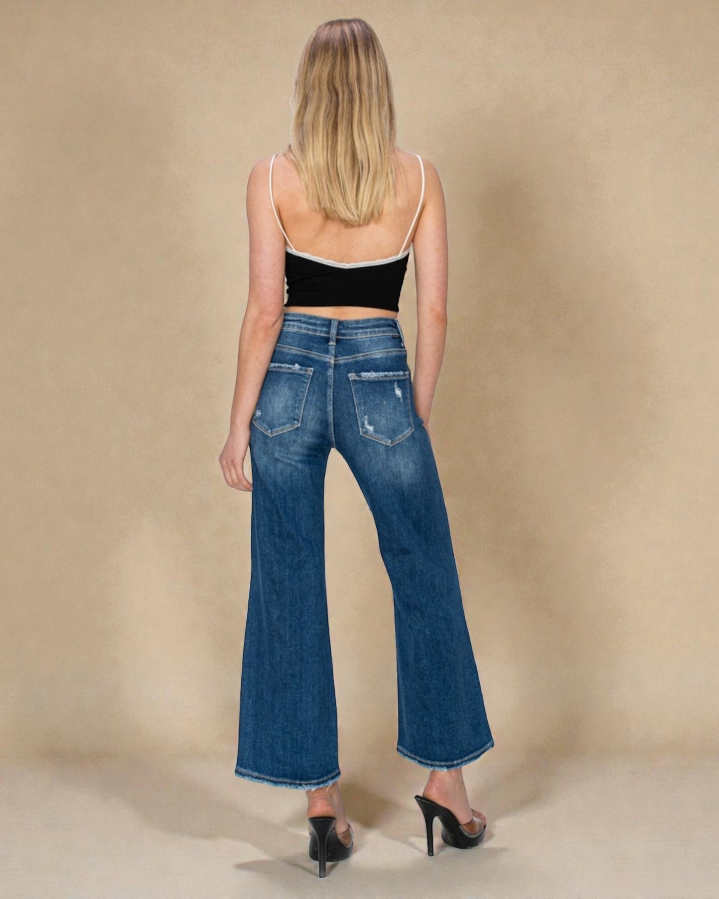Woman wearing blue jeans and a black top against a beige background