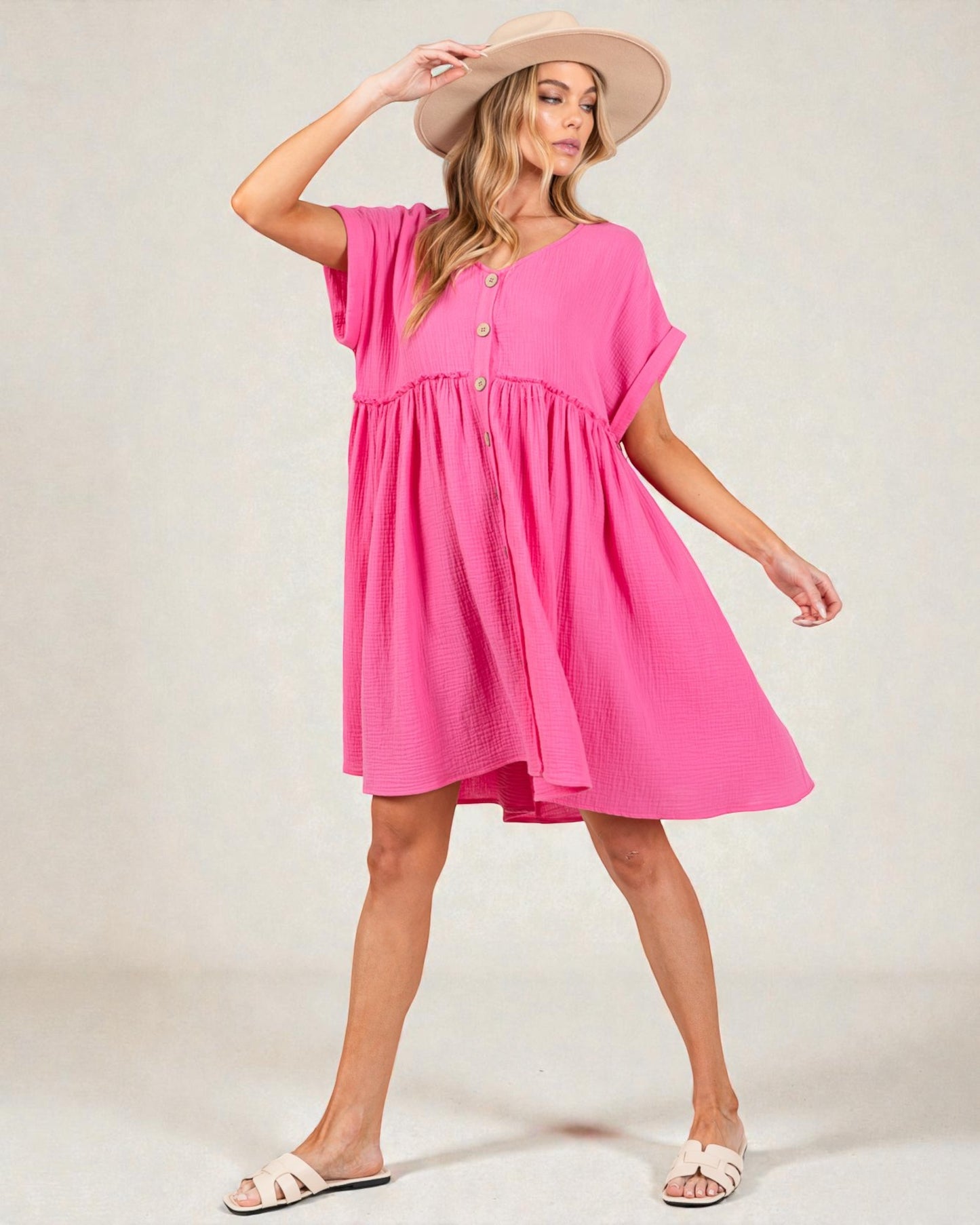 Woman wearing a pink dress and beige hat on a plain background