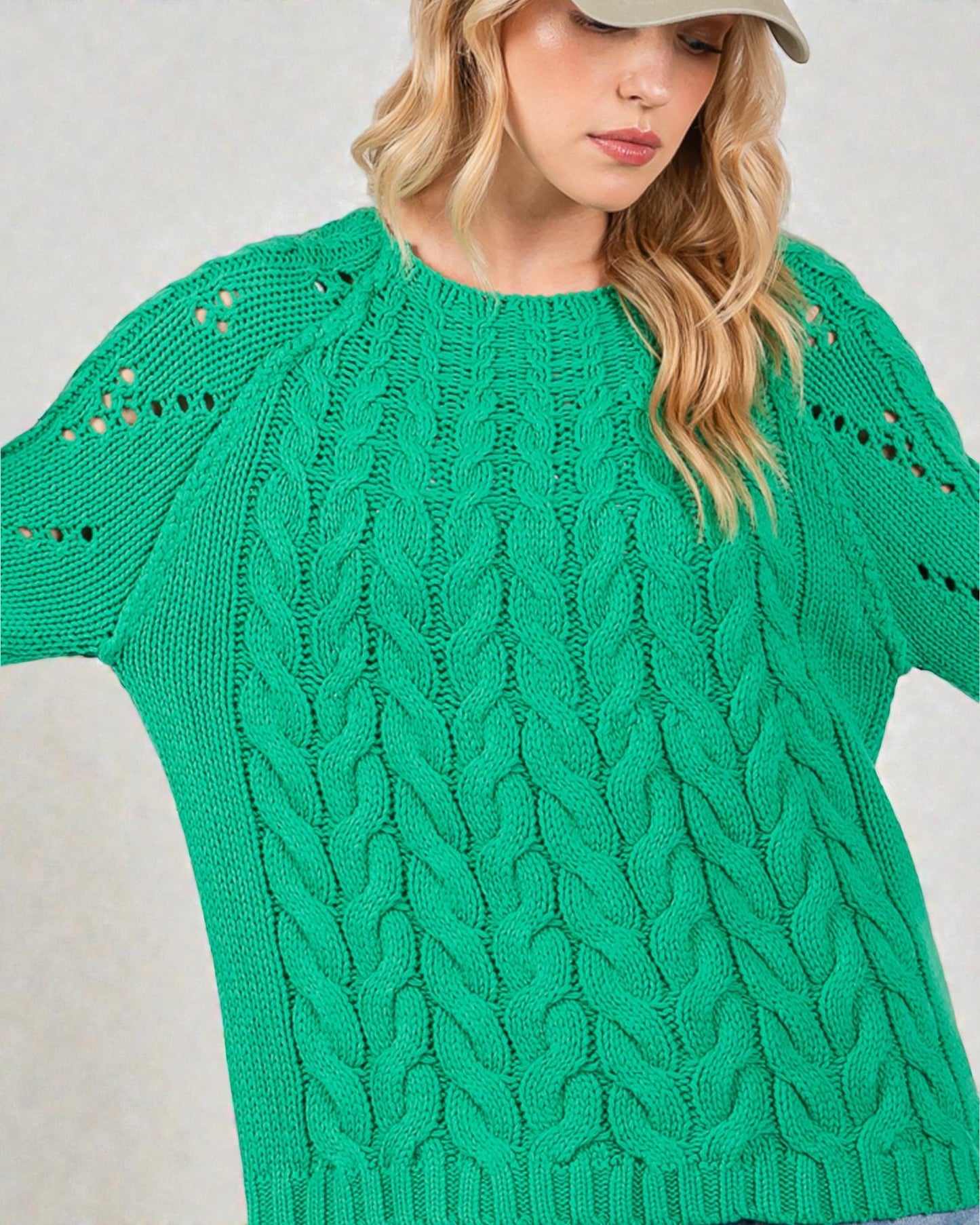 Woman wearing a green cable knit sweater against a neutral background