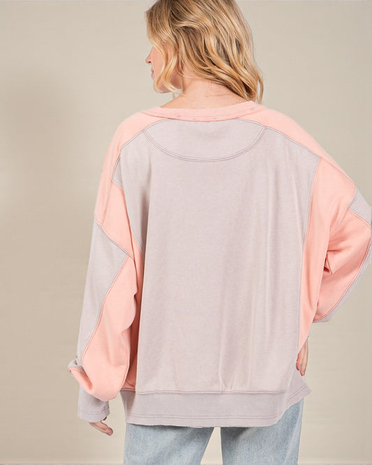 Person wearing a pink and gray color-blocked sweater on a beige background