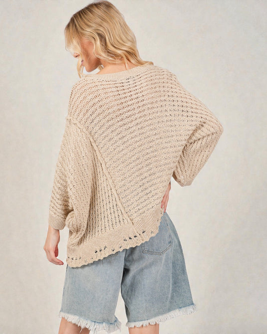 Woman wearing a beige knitted sweater and denim shorts on a plain background