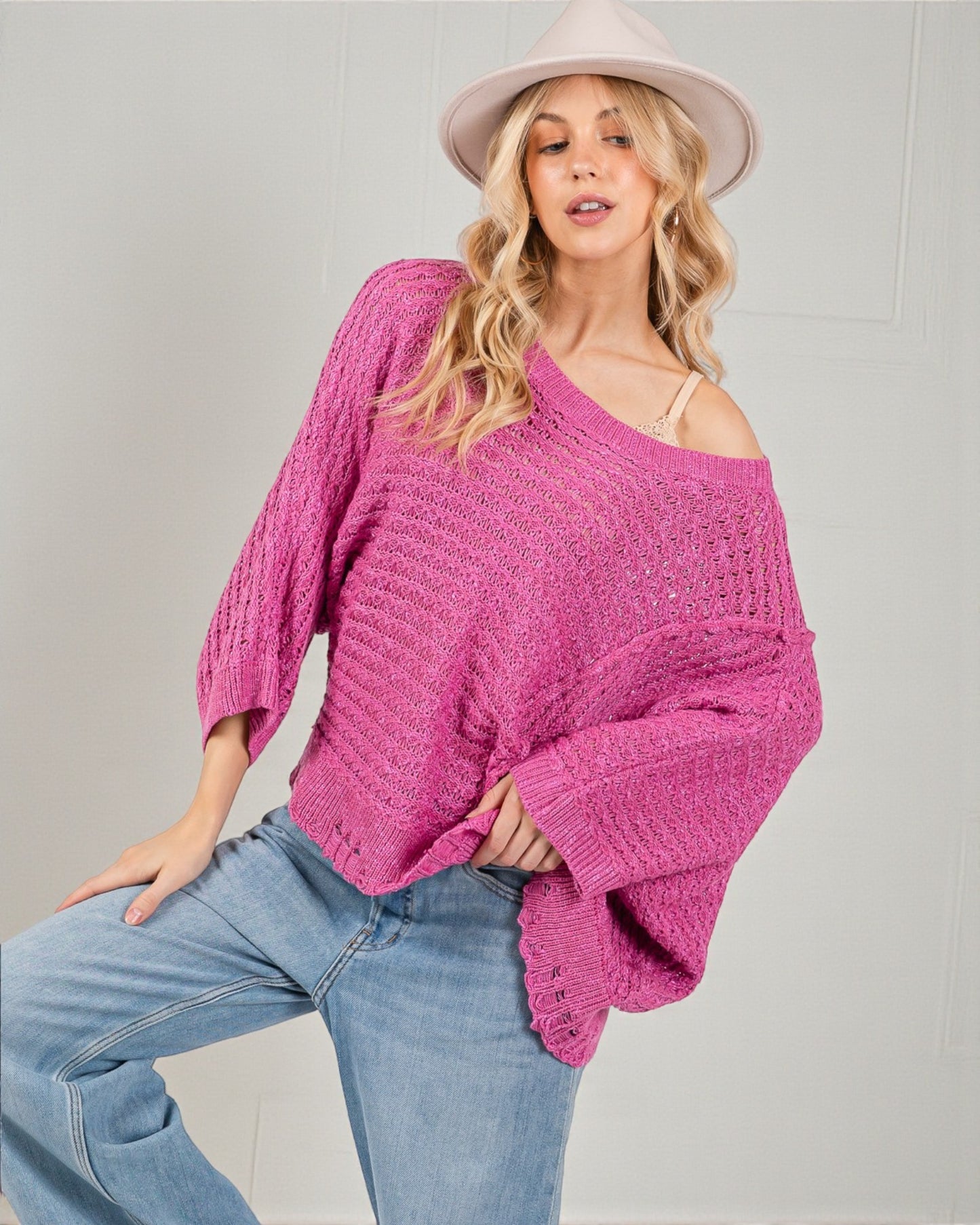 Woman wearing a pink knitted sweater and light blue jeans against a plain background